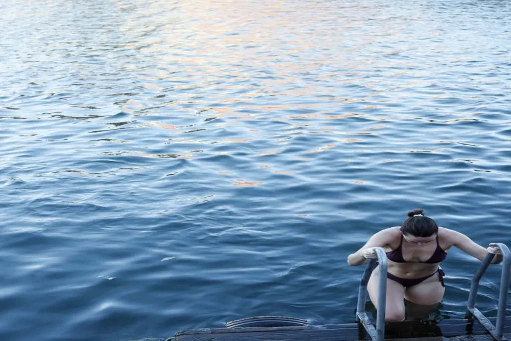Woman stepping out of cold water after a cold plunge session, supporting recovery, energy and resilience.
